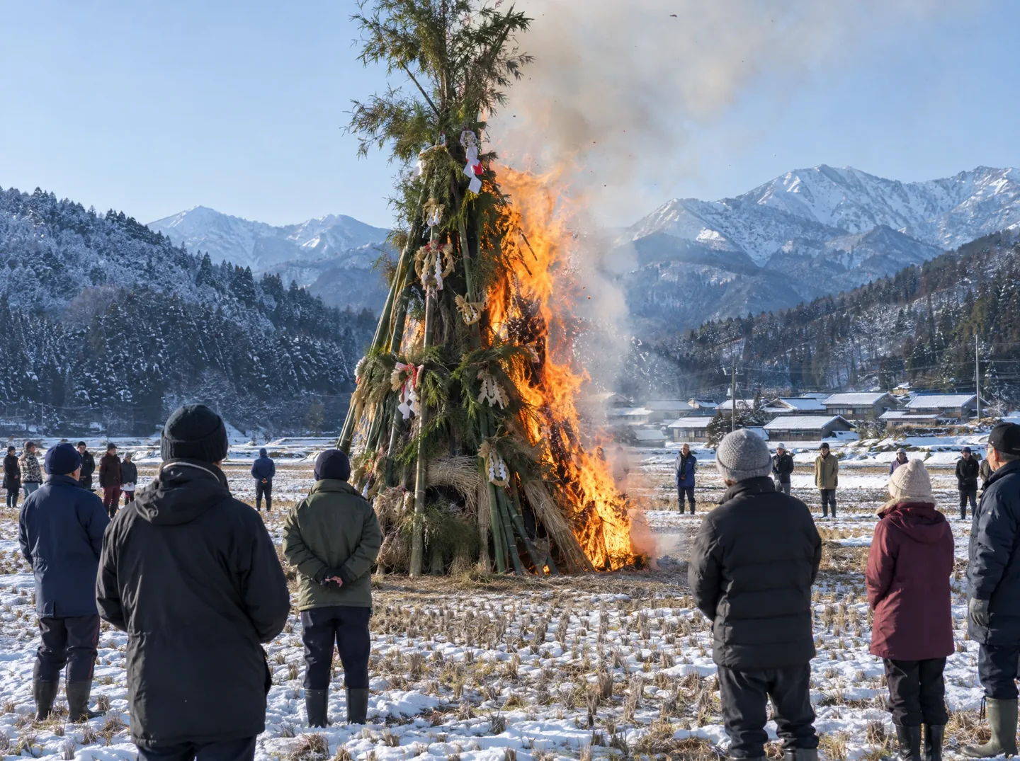 A tall conical bonfire of bamboo and straw New Year decorations burning in a snowy field, with villagers in winter coats standing around it and mountains behind.